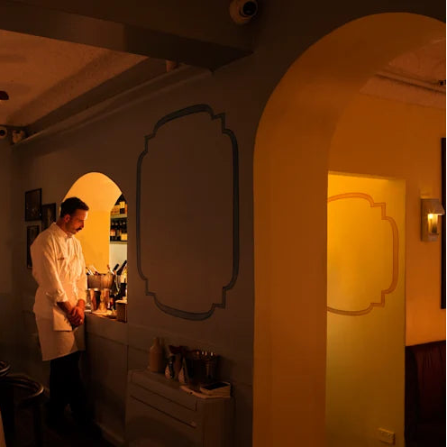 Dining area with a chef in a restaurant setting, featuring the PARCTA Egress Sconce.